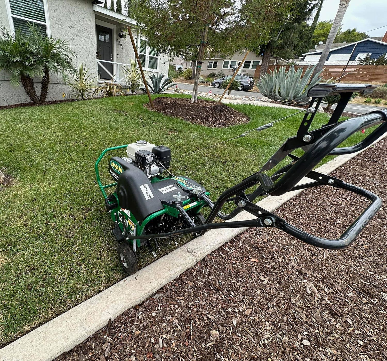 A lawn mower is parked on the side of the road next to a lush green lawn.