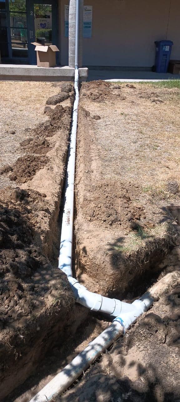 A drain pipe is being installed in the dirt next to a house.