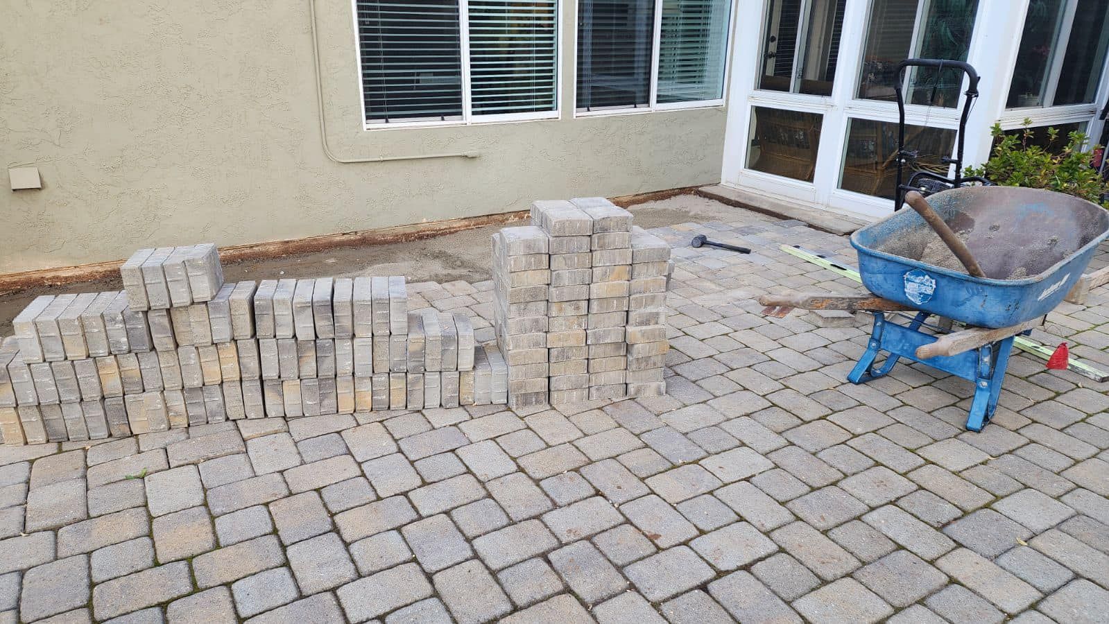 A wheelbarrow is sitting on a brick patio next to a pile of bricks.