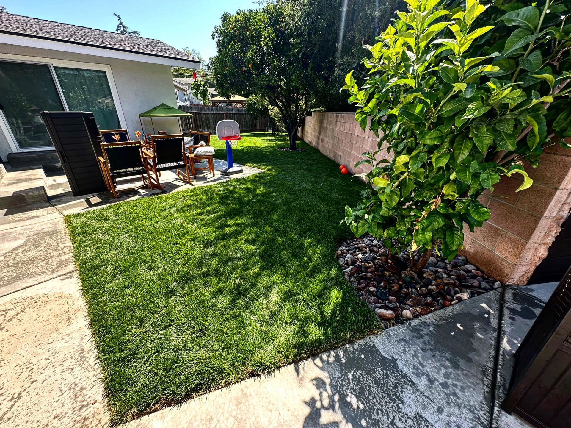 A backyard with a lush green lawn and a patio area with a table and chairs.