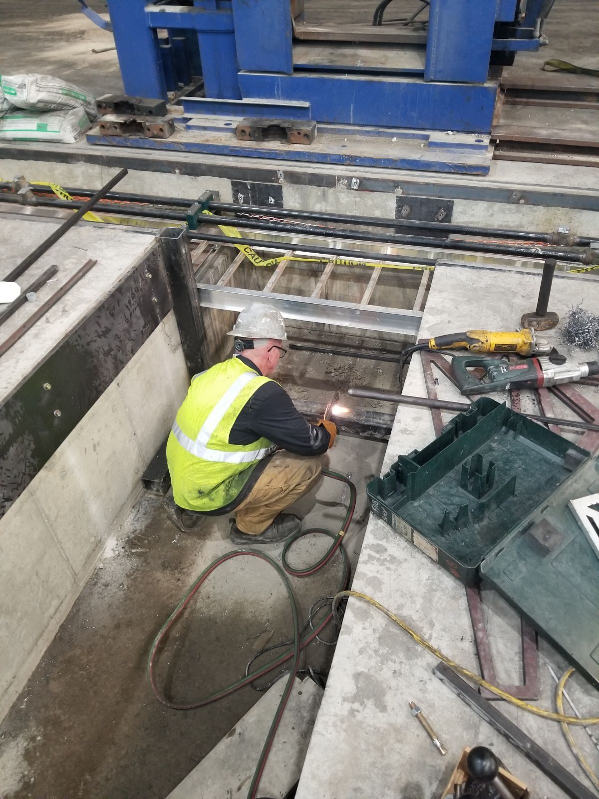 A man in a yellow vest is welding a piece of metal.