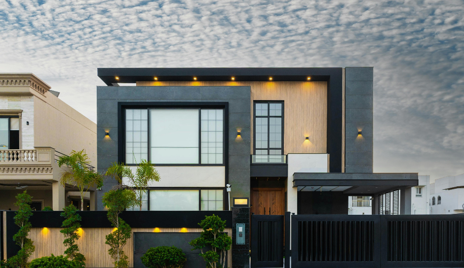 Modern home exterior with gray and wood accents; black gate and cloudy sky.