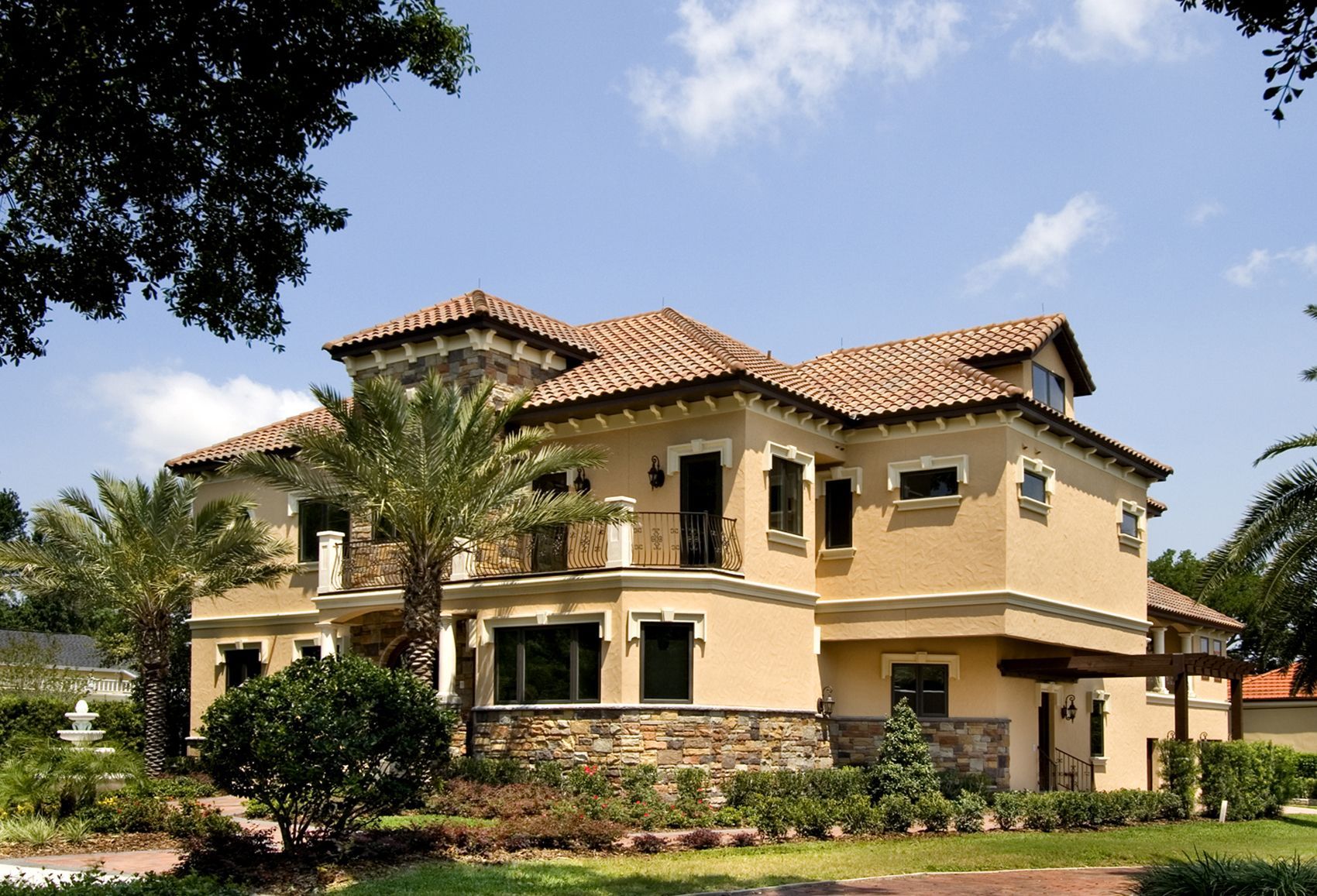 A large house with a tiled roof is surrounded by palm trees