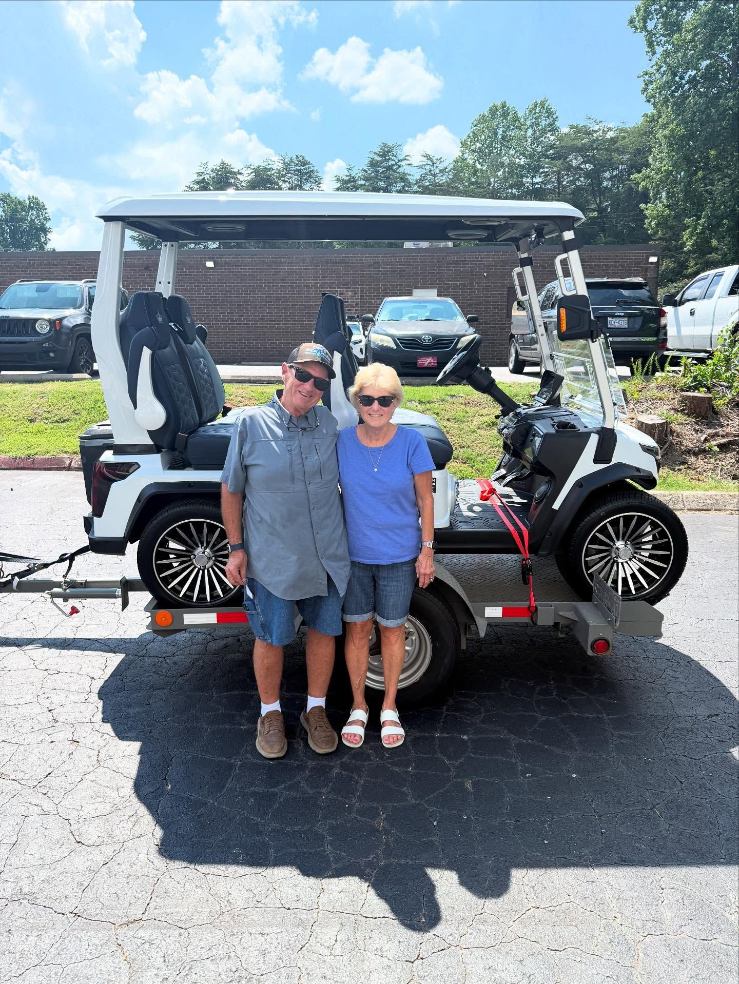 A man and woman are standing in front of a golf cart.