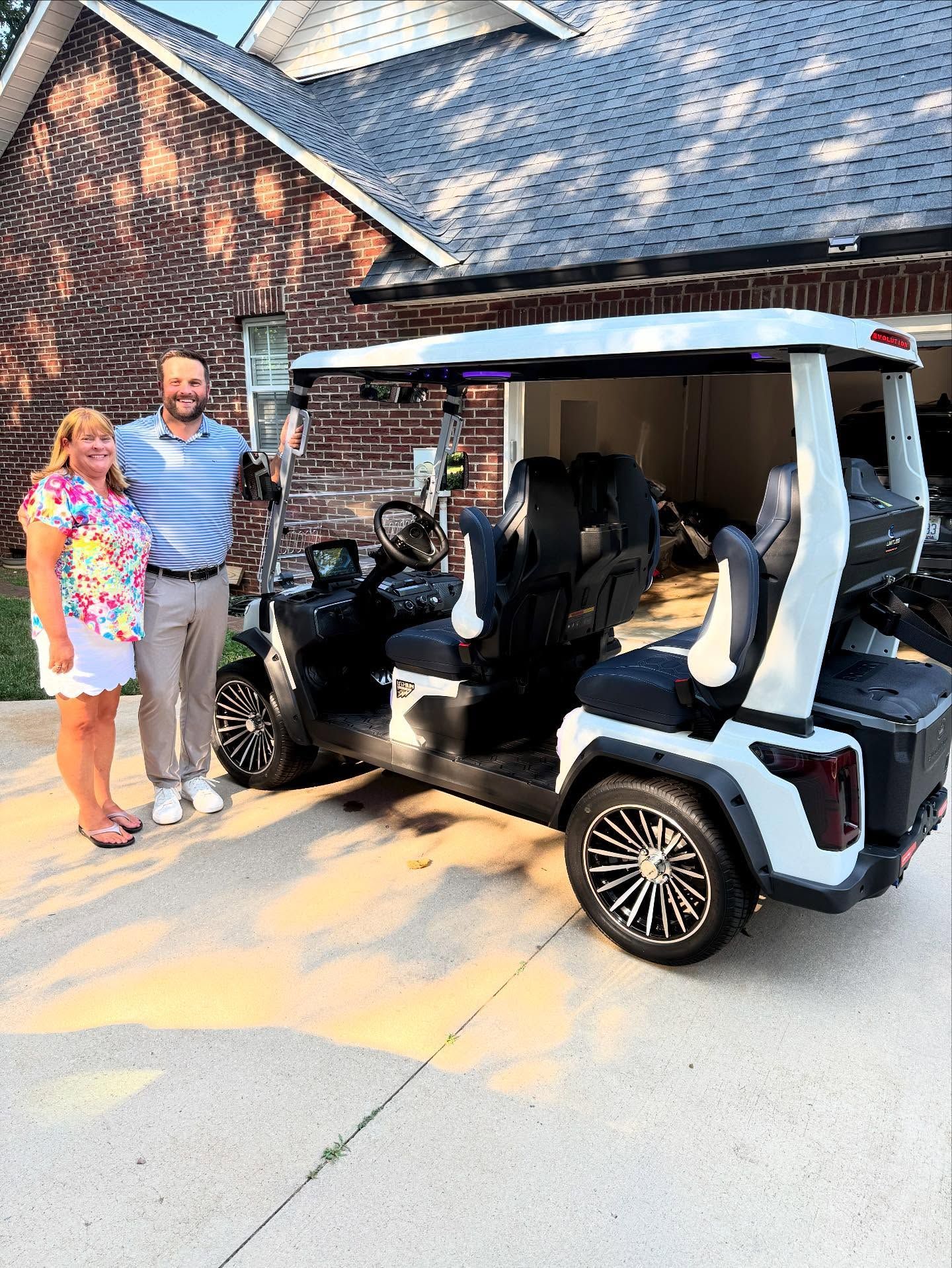 A man and a woman are standing in front of a golf cart.