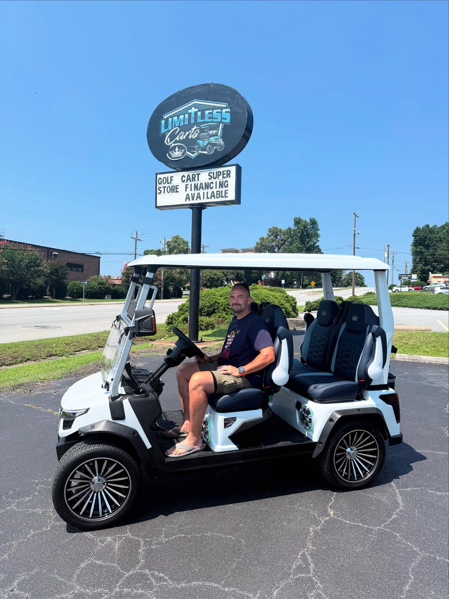 A man is sitting in a white golf cart in front of a sign.