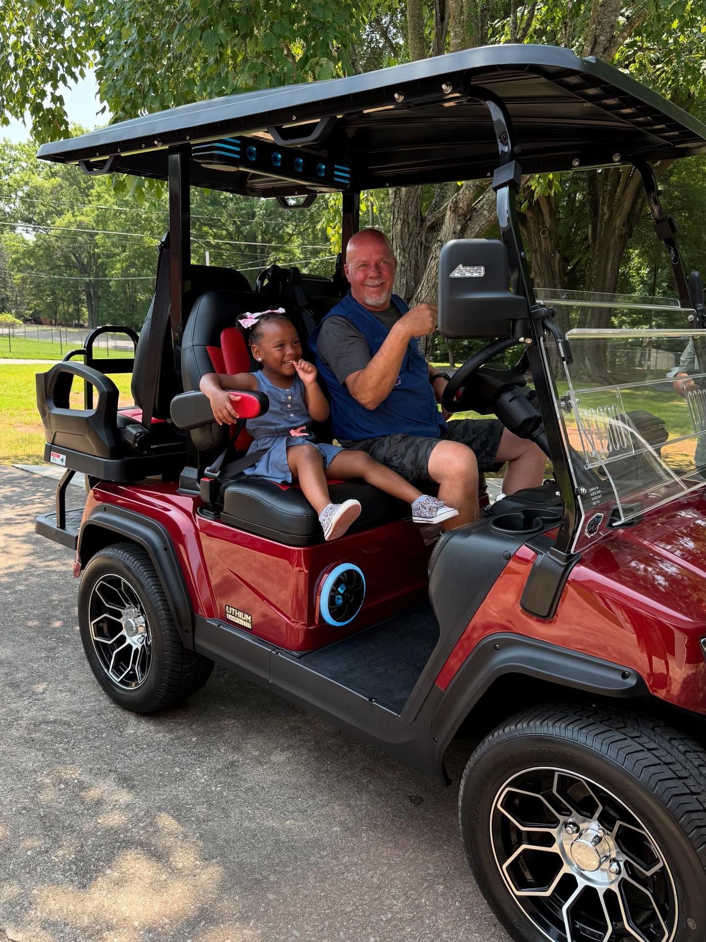 A man and a little girl are sitting in a golf cart.