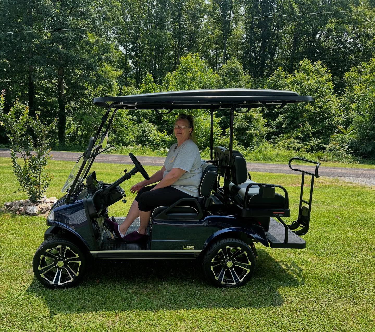 A man is sitting in a golf cart on a lush green field.