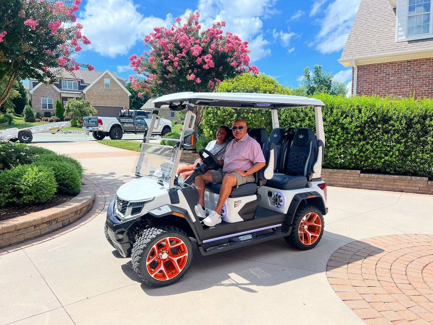 Two people are riding in a golf cart in a driveway.