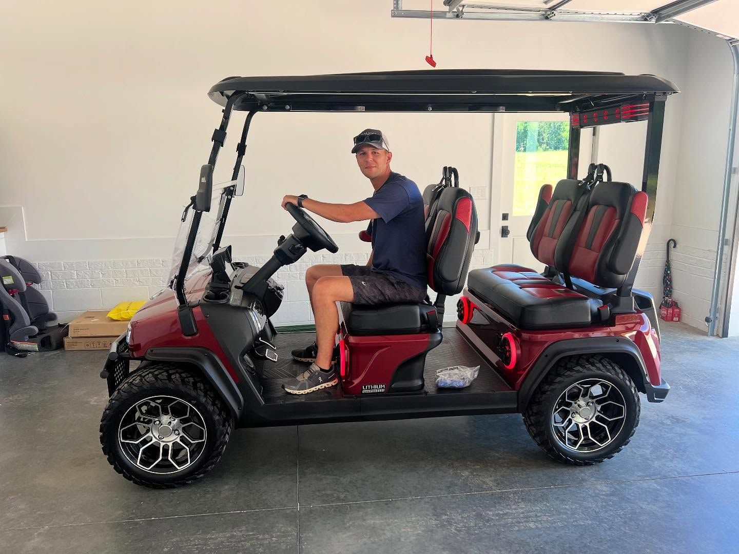A man is sitting in a red golf cart in a garage.