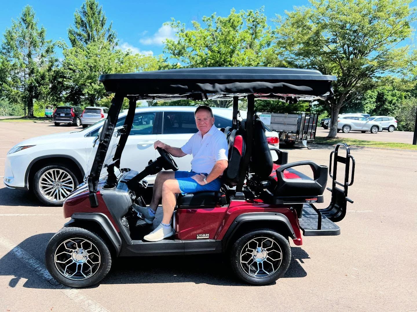 A man is sitting in a red golf cart in a parking lot.