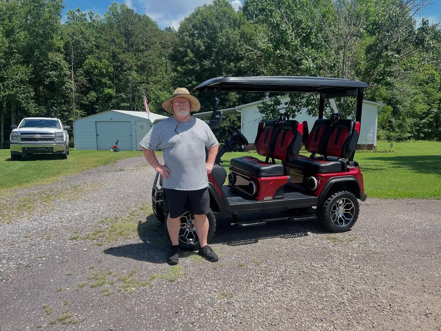 A man in a hat is standing next to a red golf cart.