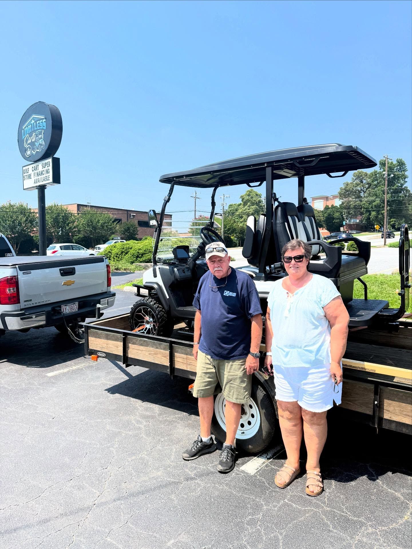 A man and a woman are standing next to a golf cart on a trailer.