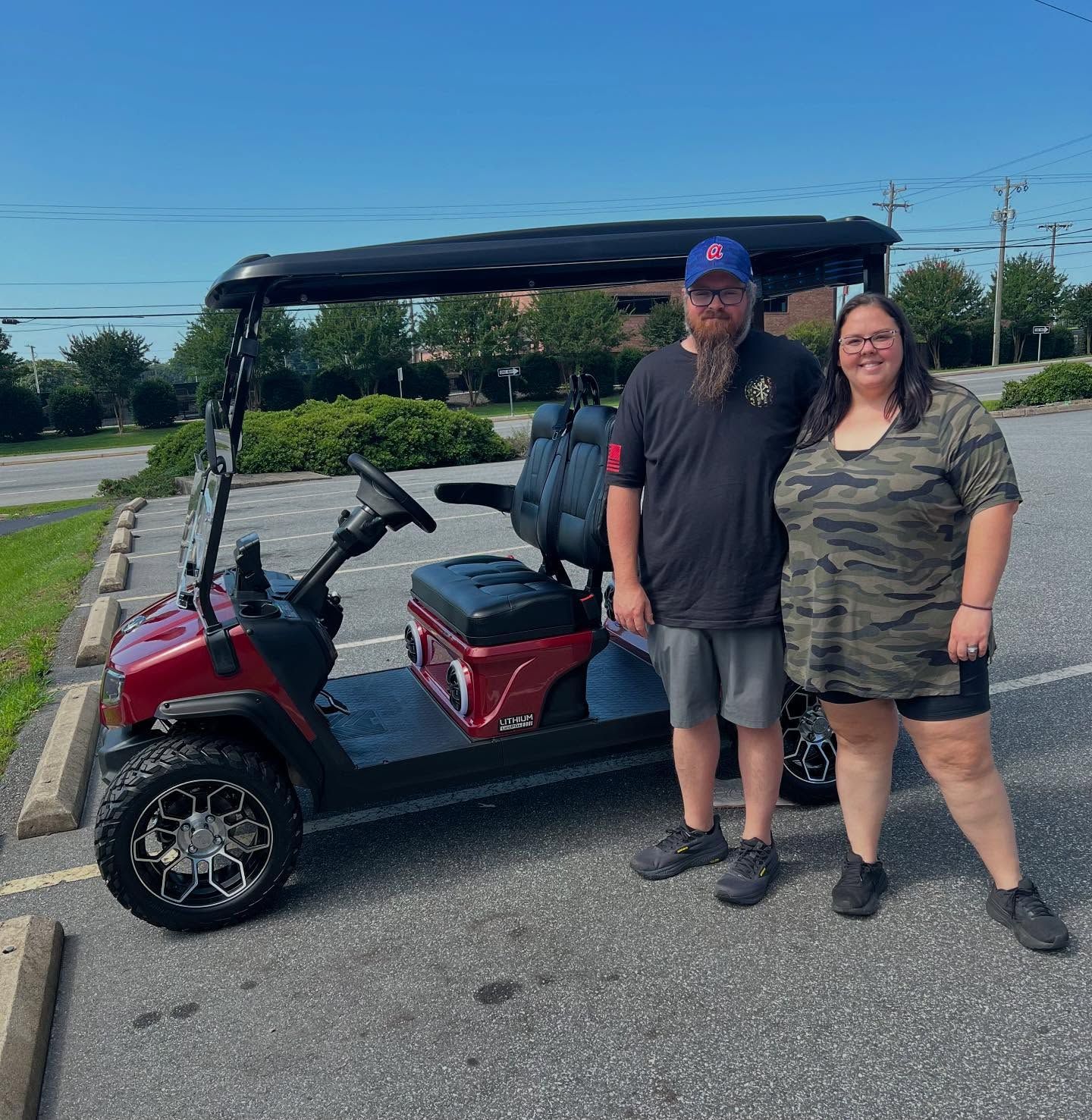 A man and a woman are standing next to a golf cart in a parking lot.