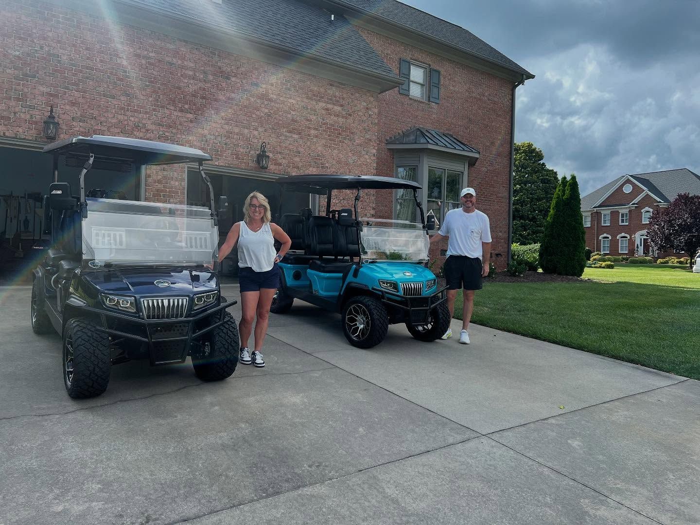 A man and a woman are standing in front of two golf carts in a driveway.
