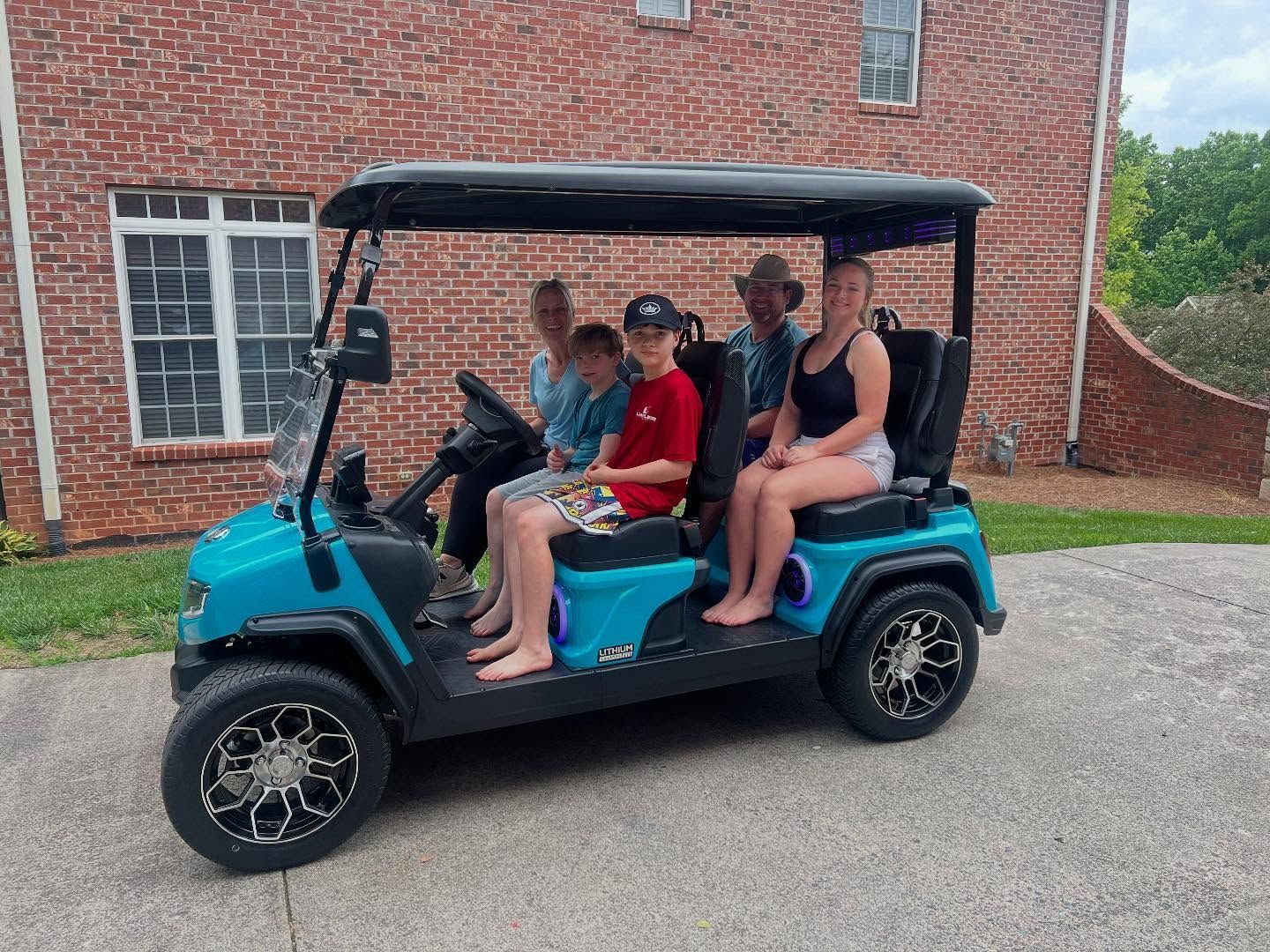 A family is sitting in a blue golf cart in front of a brick house.