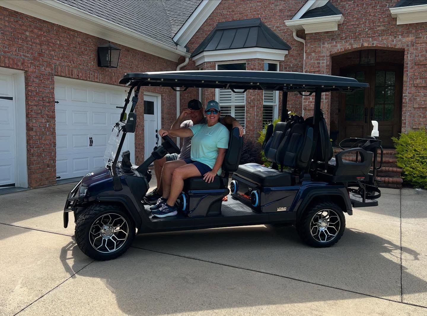 Two people are sitting in a golf cart parked in front of a brick house.