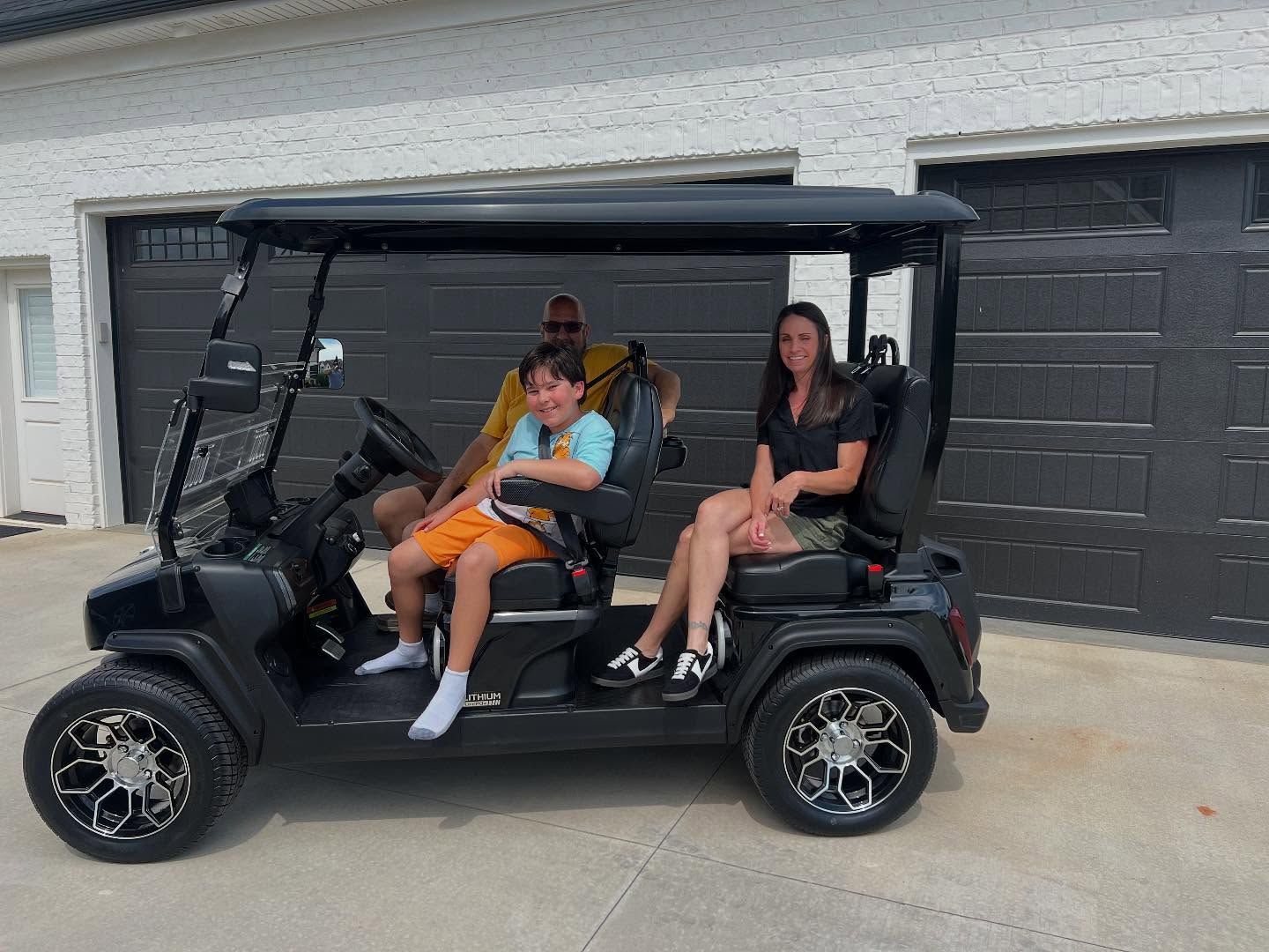A family is sitting in a black golf cart in front of a garage.