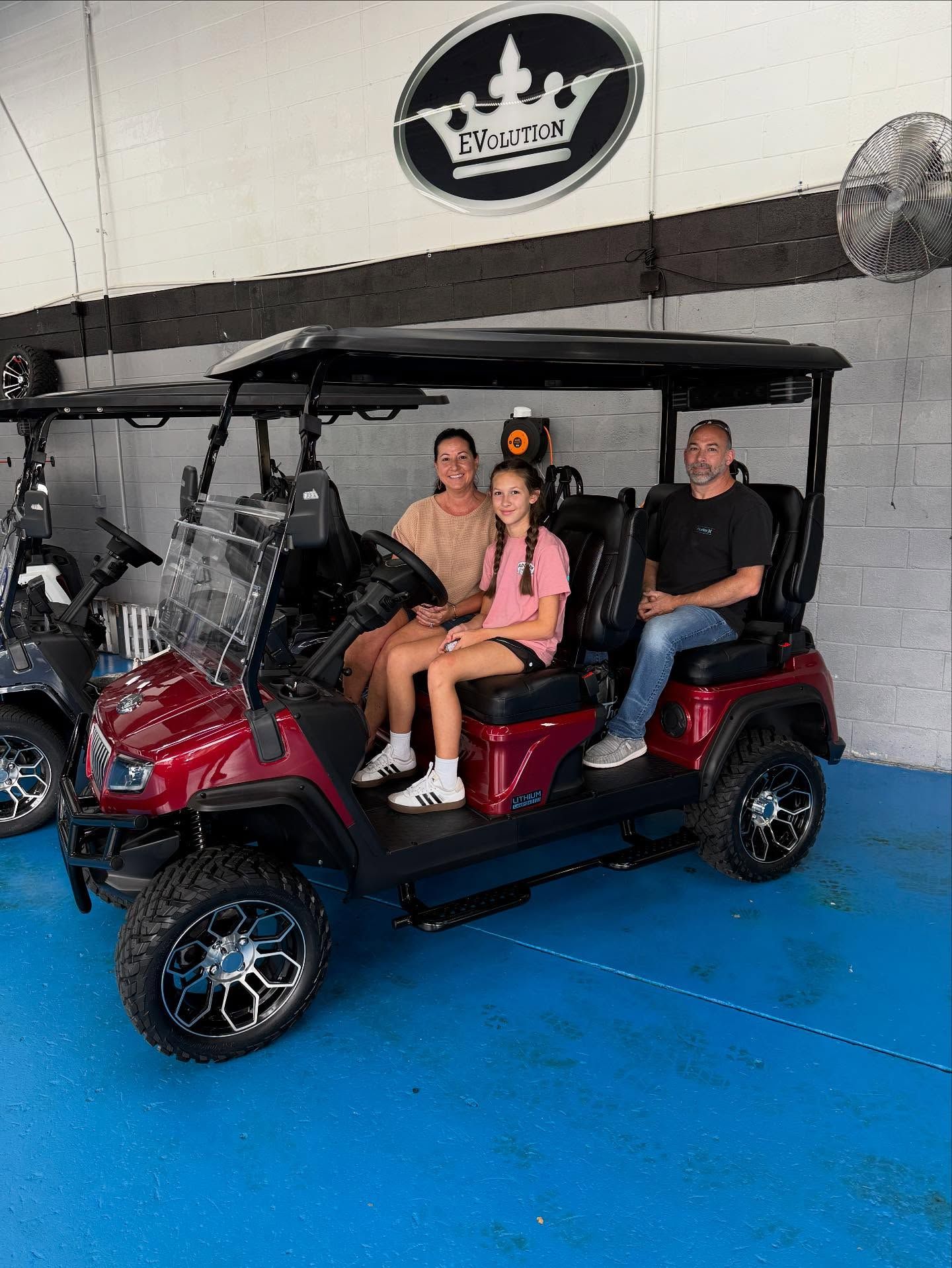 A family is sitting in a golf cart in a showroom.