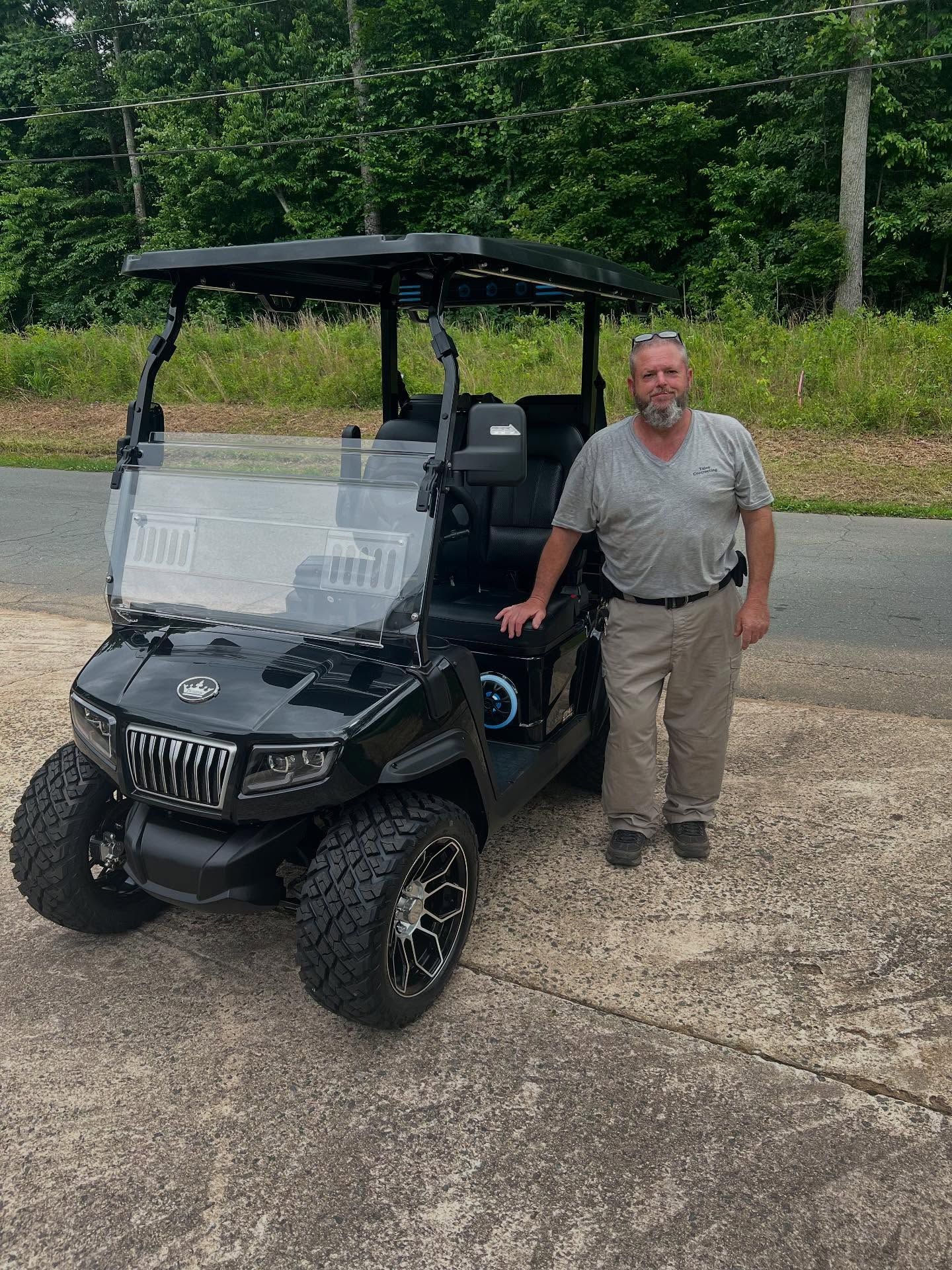 A man is standing next to a black golf cart.