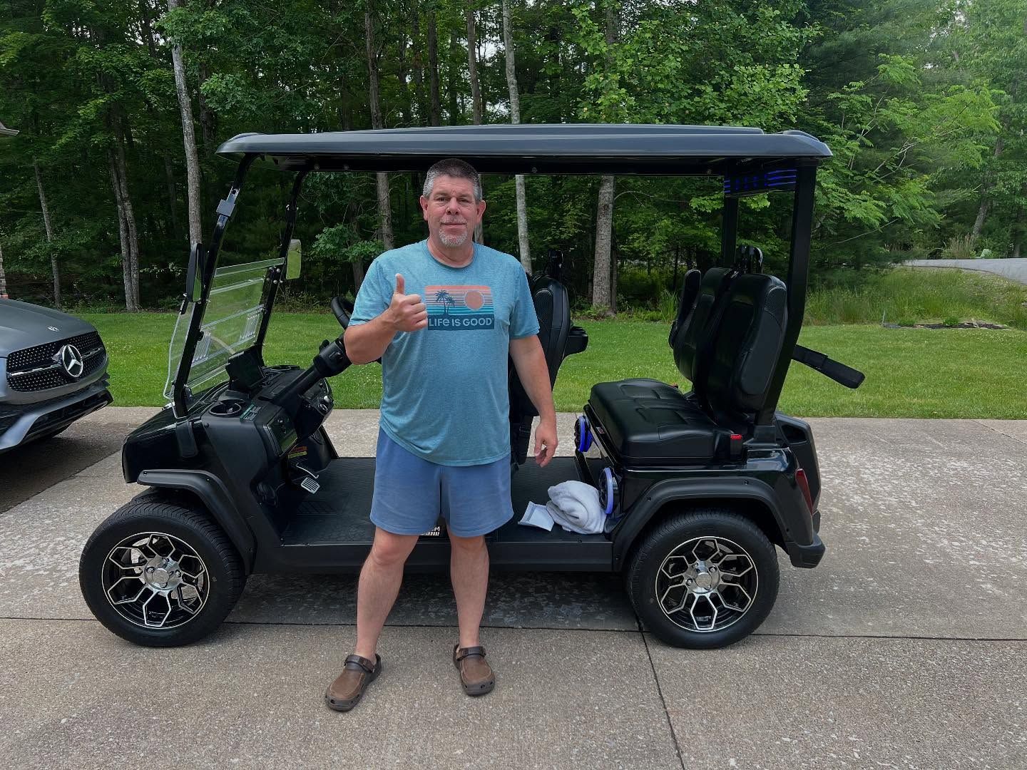 A man is standing in front of a golf cart giving a thumbs up.