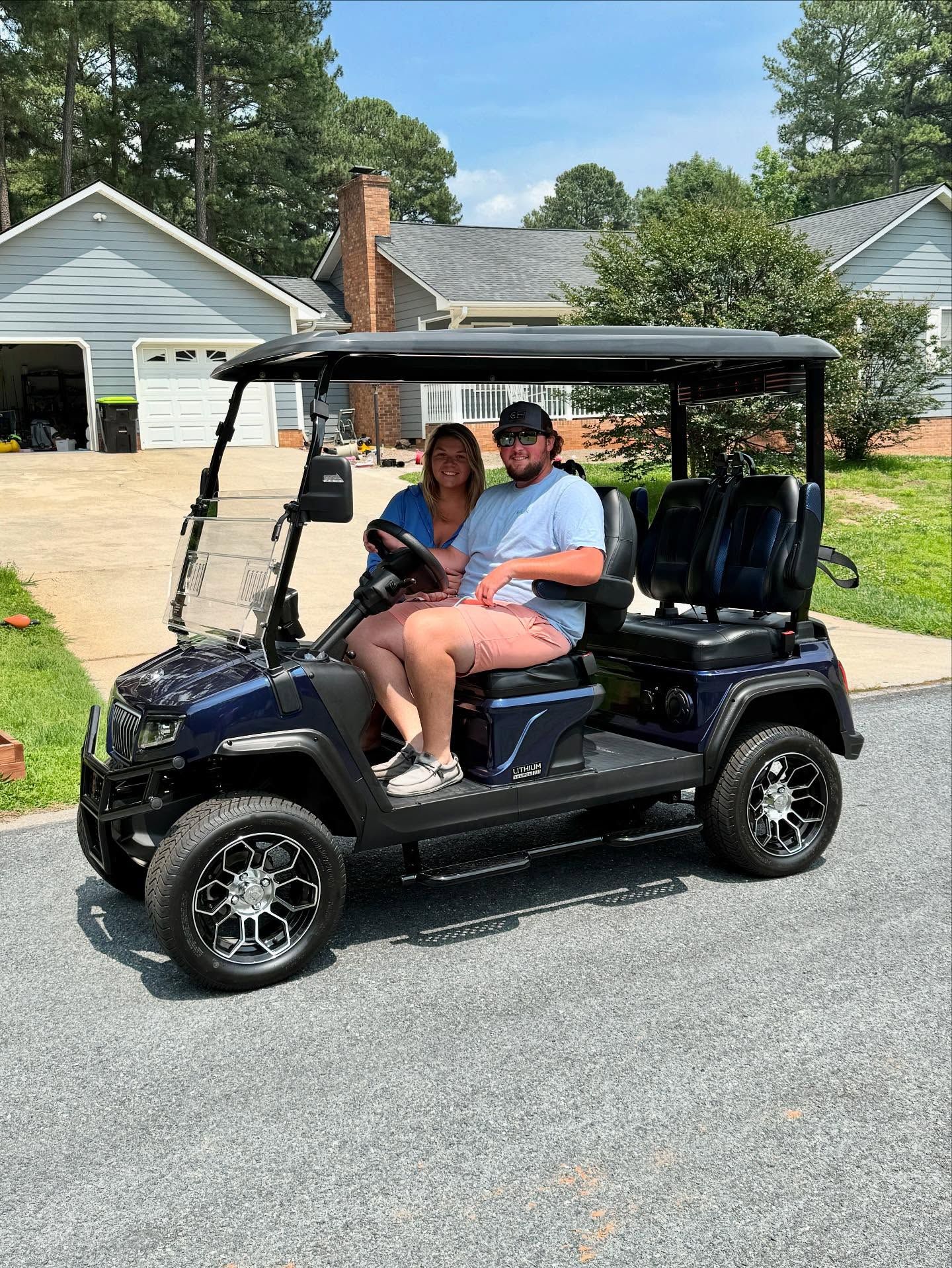 A man and a woman are sitting in a golf cart in front of a house.