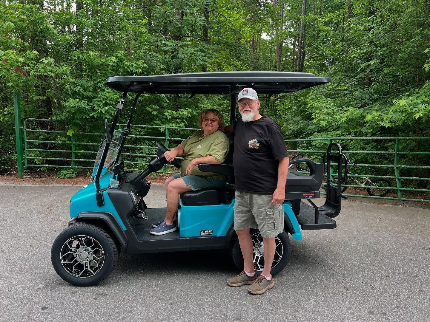 A man and a woman are standing next to a blue golf cart.