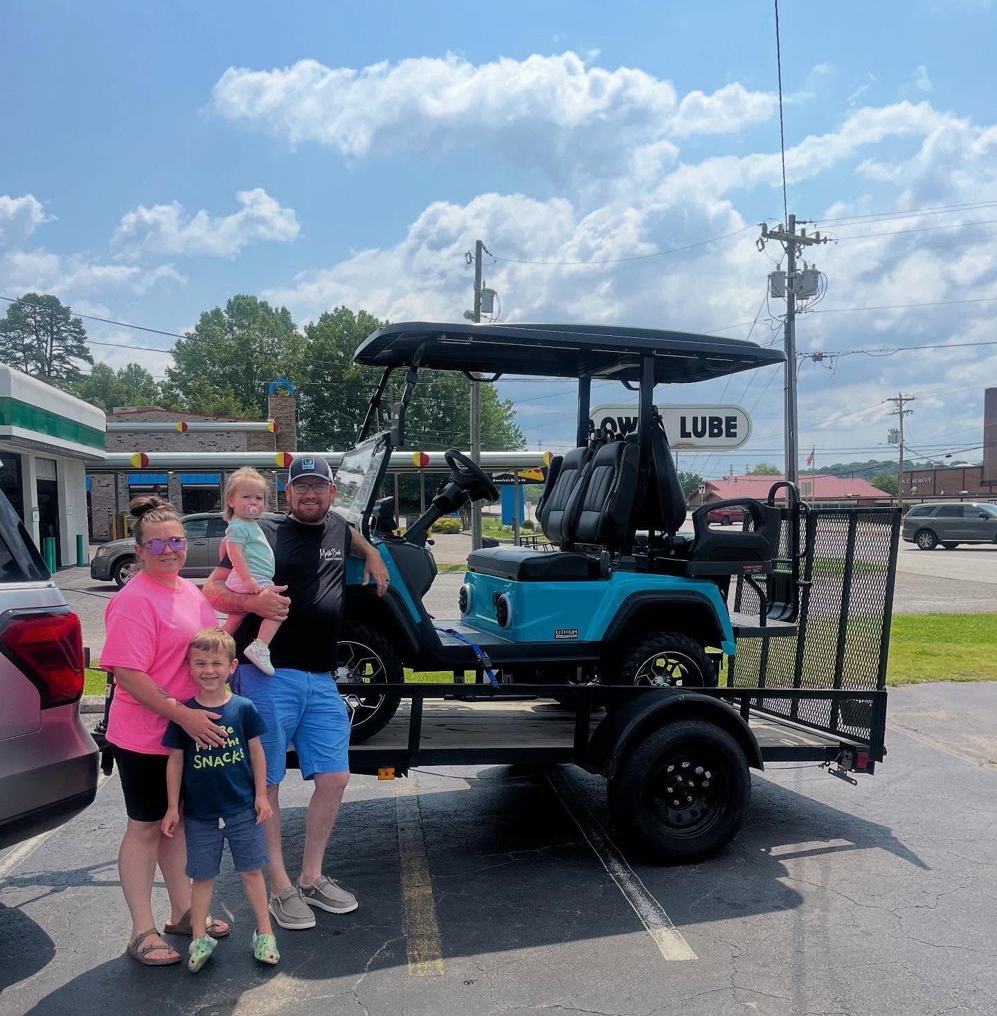 A family standing in front of a golf cart that says lube on it