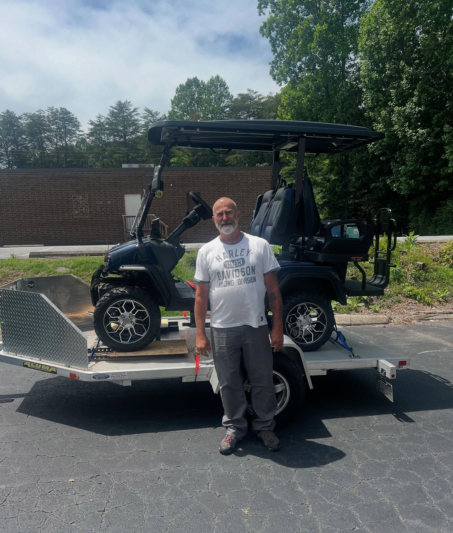 A man is standing in front of a golf cart on a trailer