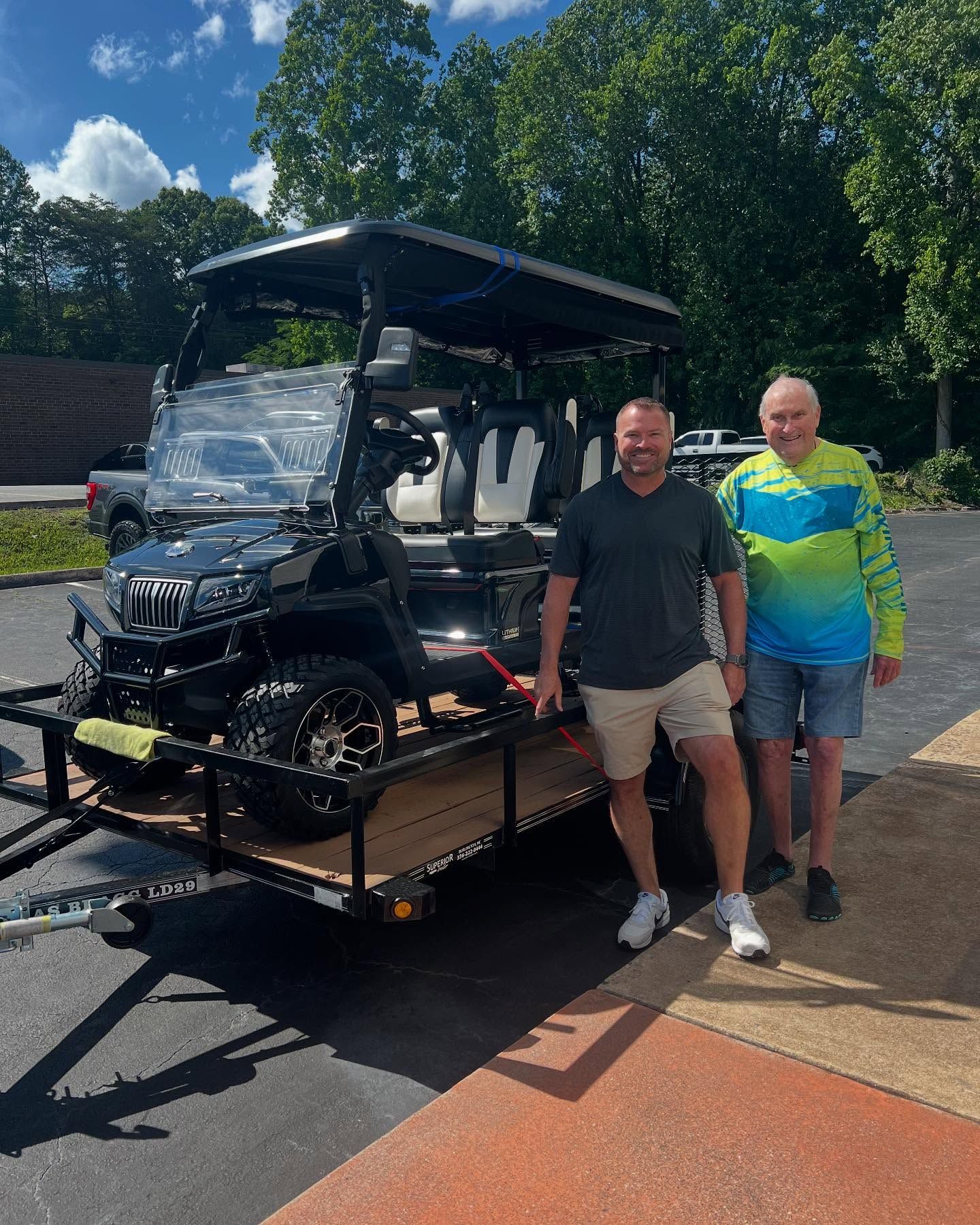 Two men are standing next to a golf cart on a trailer.