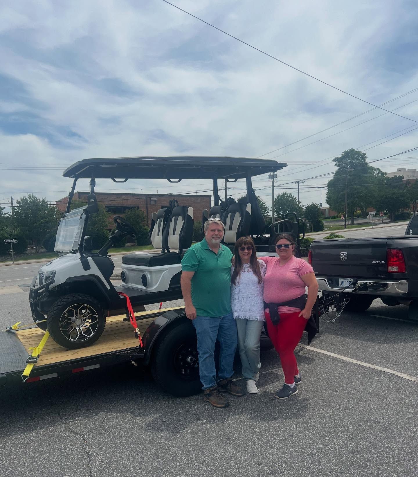 Three people are standing in front of a golf cart on a trailer.