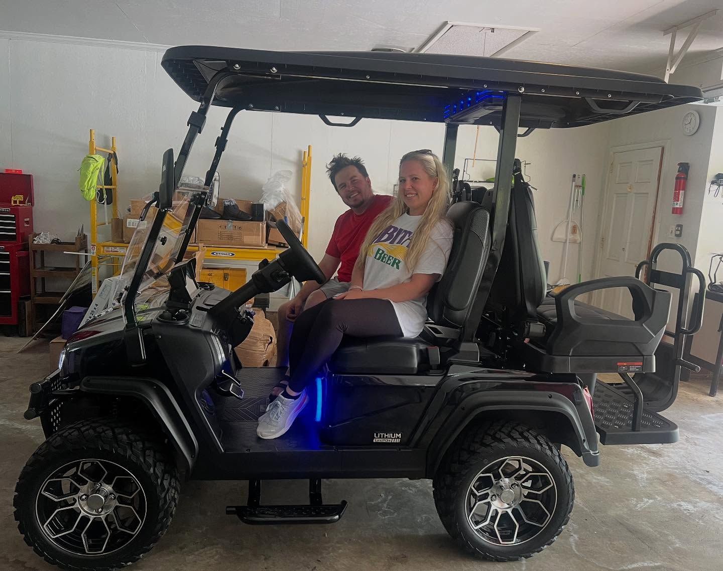 A man and a woman are sitting in a golf cart in a garage.