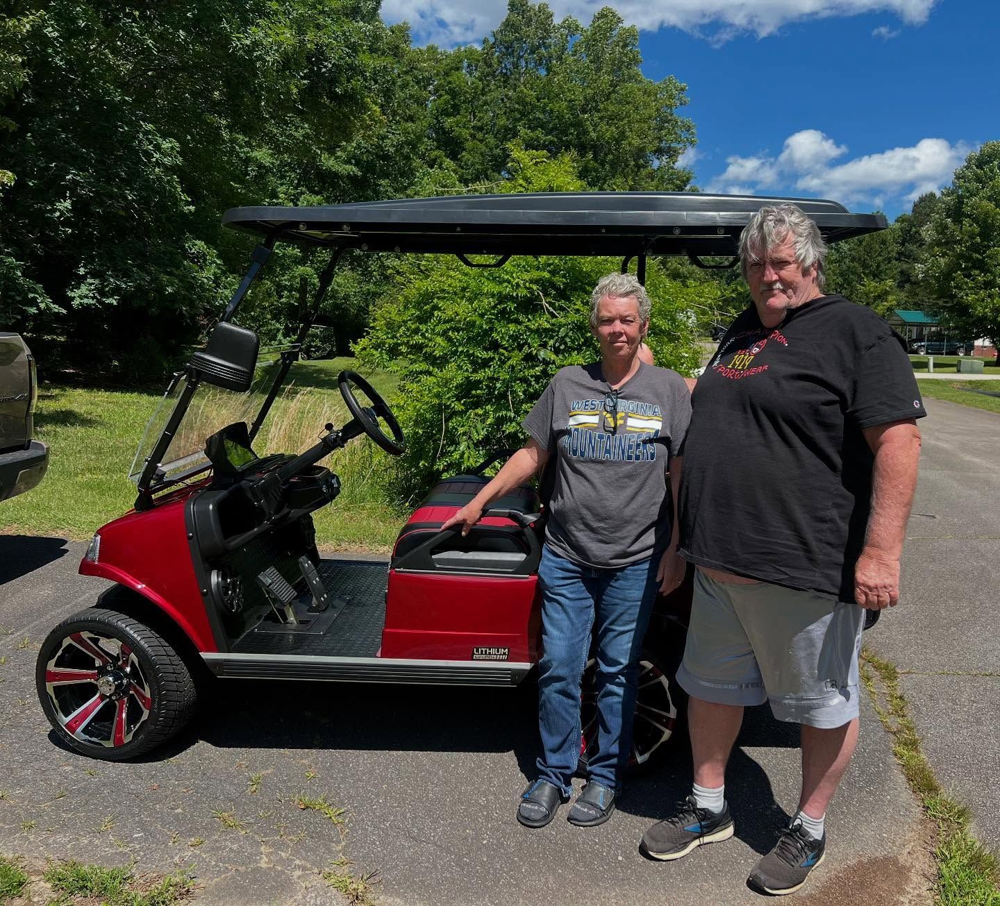 Two men are standing next to a red golf cart