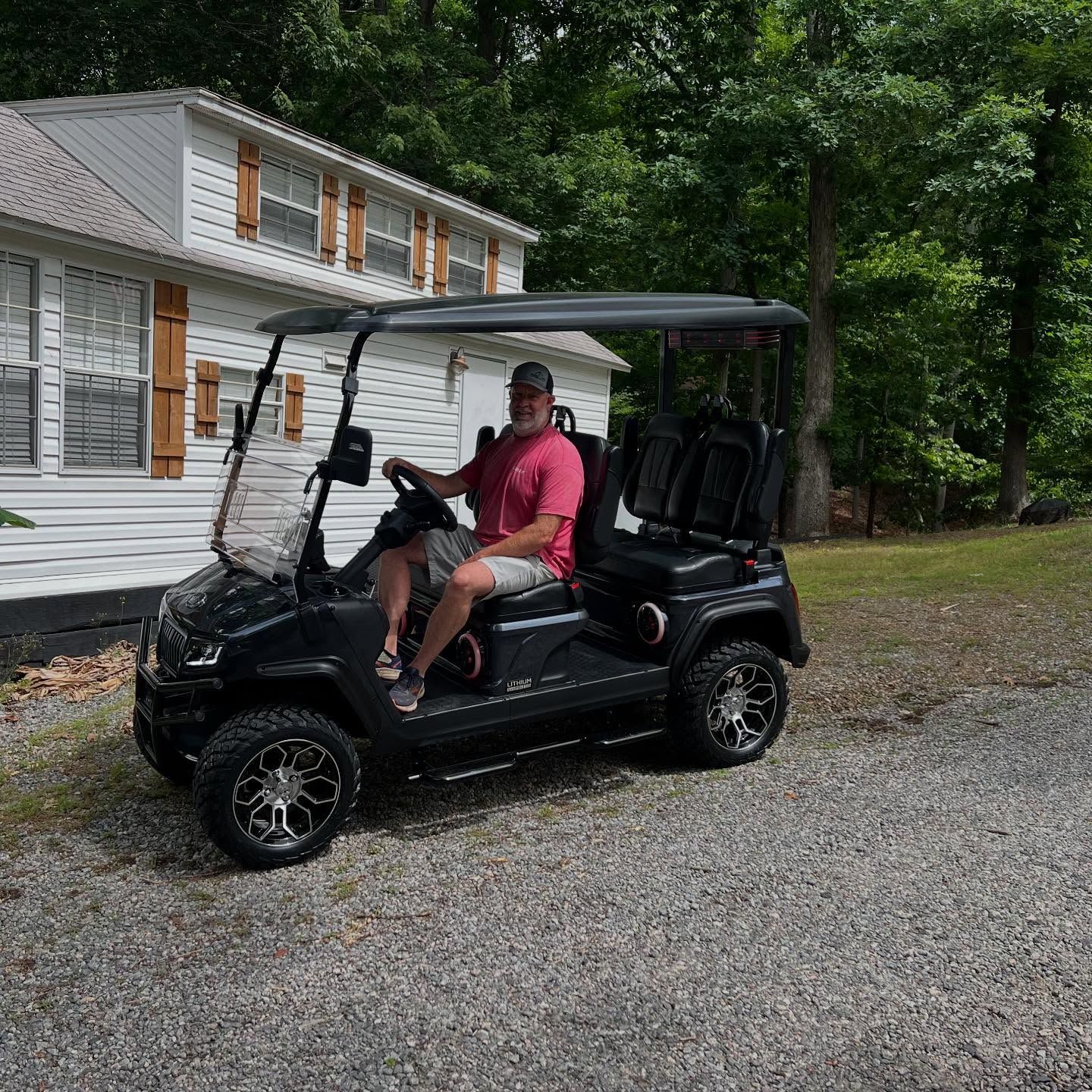 A man is driving a golf cart in front of a house.