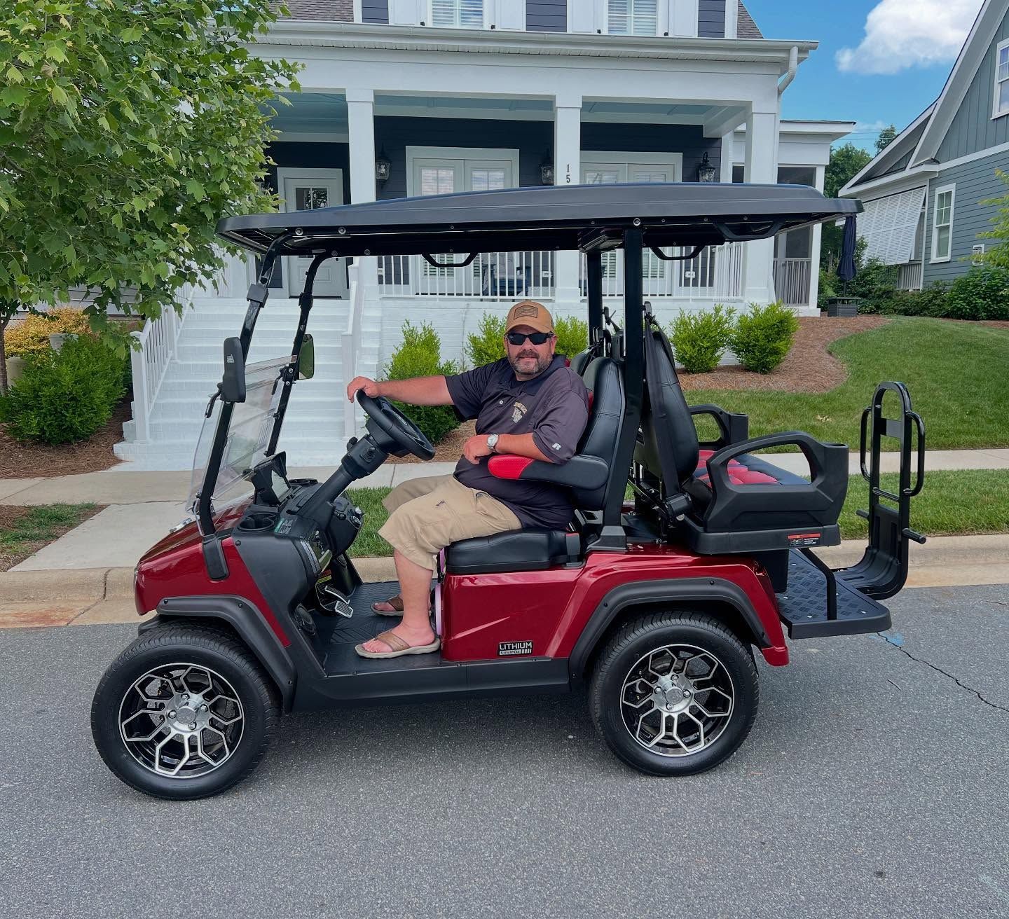 A man is driving a red golf cart in front of a house.