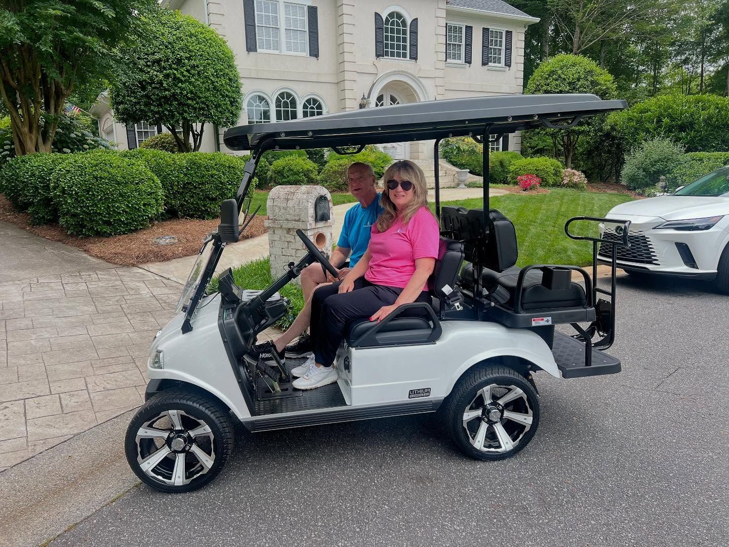 A man and a woman are sitting in a golf cart in front of a house.