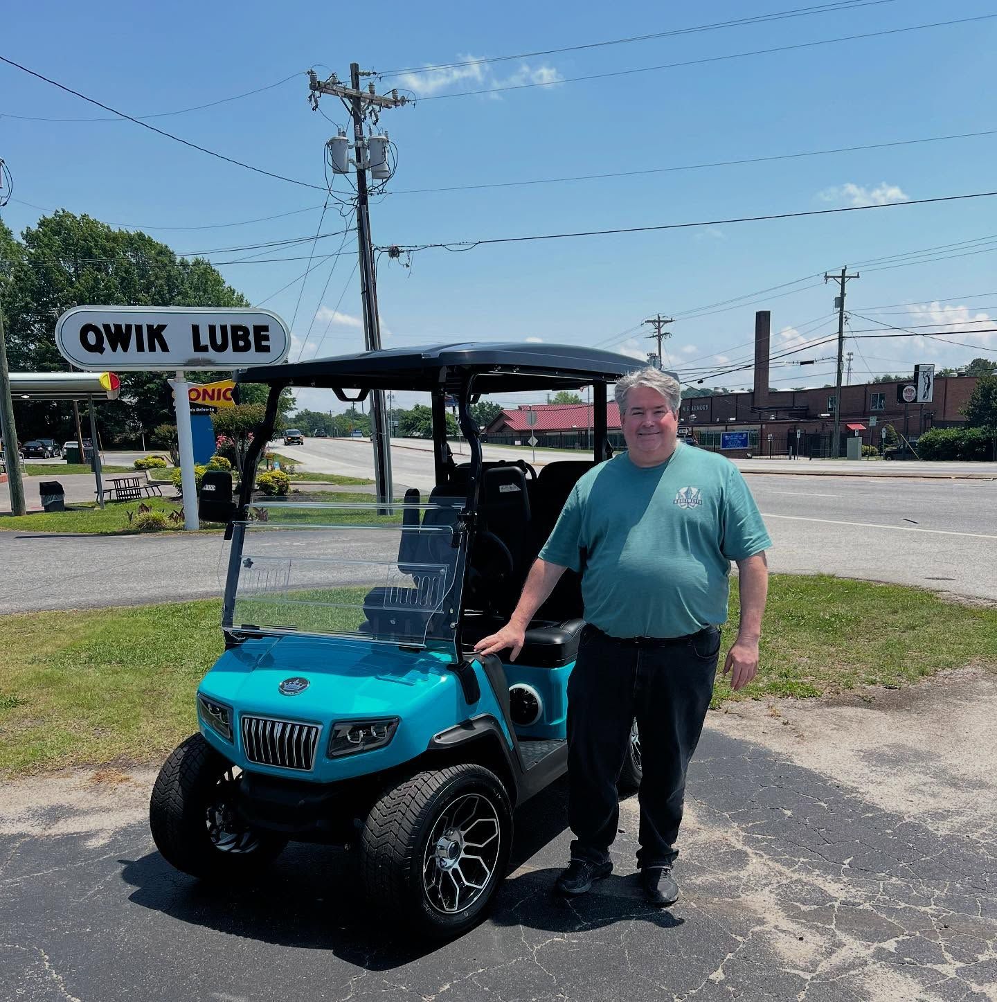 A man stands next to a blue golf cart in front of a sign that says qwik lube