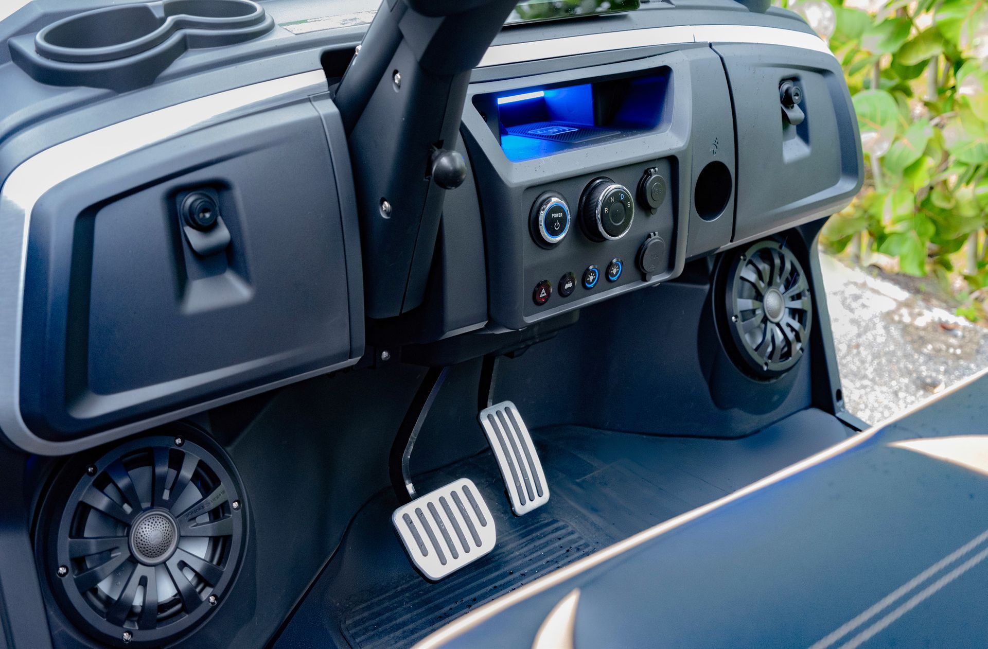 Interior of a golf cart with black dashboard, speakers, cup holders, and white pedals.