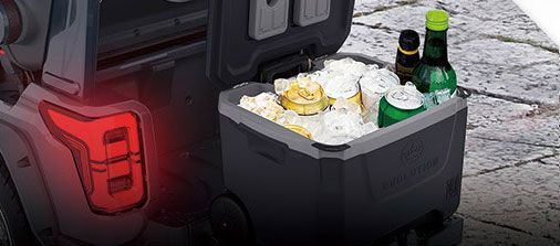 A cooler filled with beer and bottles is sitting in the back of a truck.