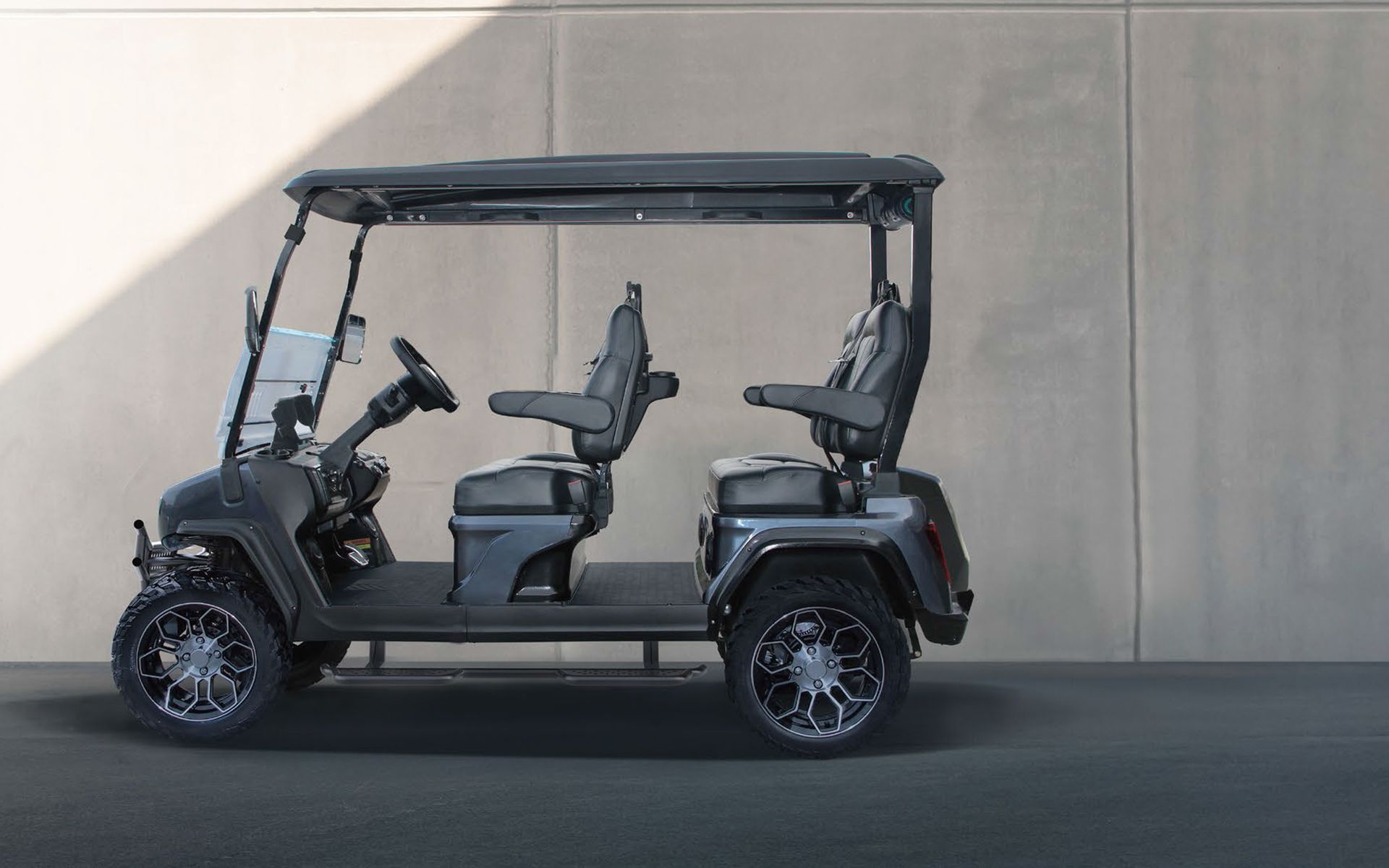 a black golf cart is parked in front of a concrete wall .