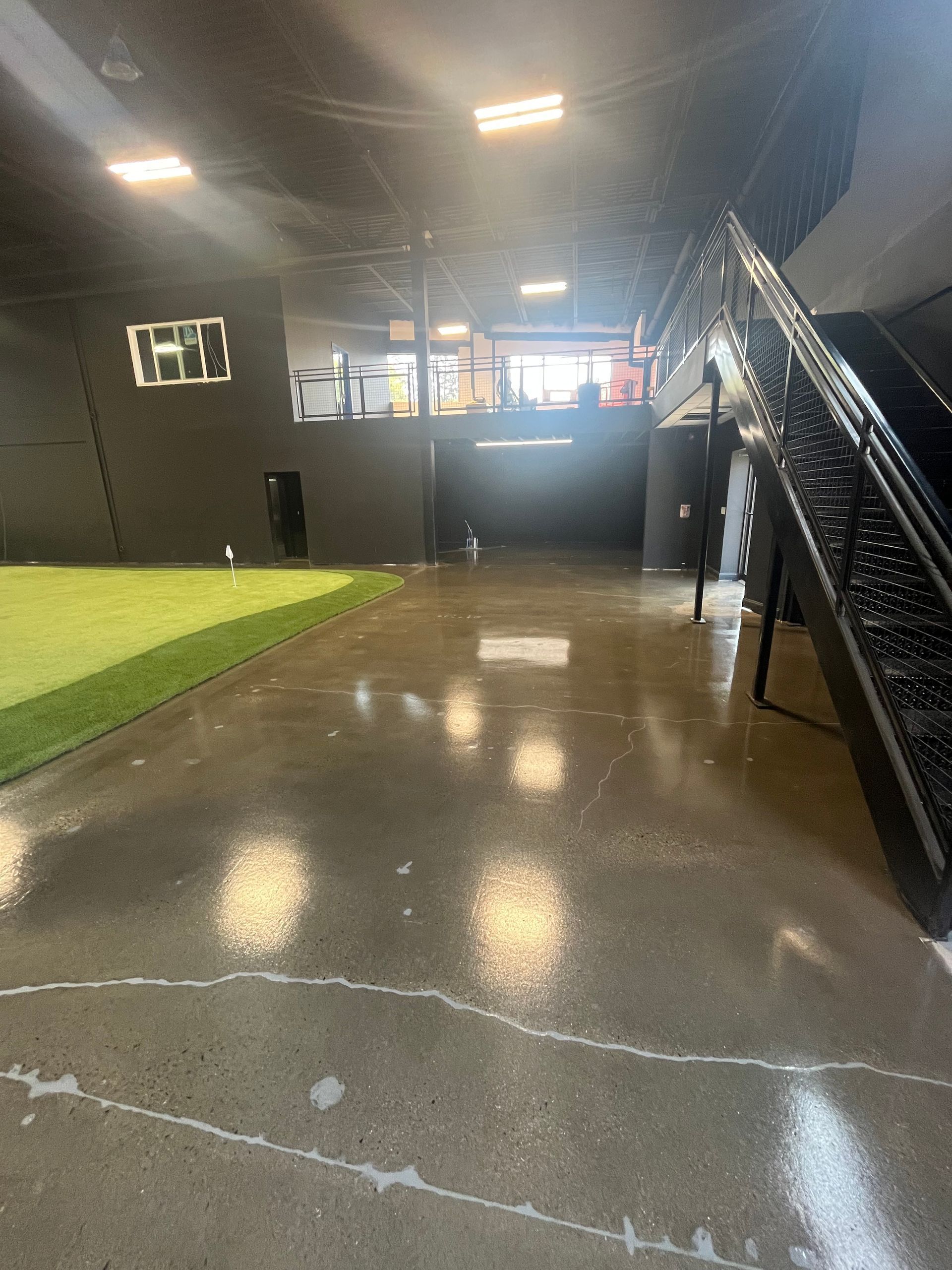 Indoor sports facility with polished concrete floor, stairs, and turf area.