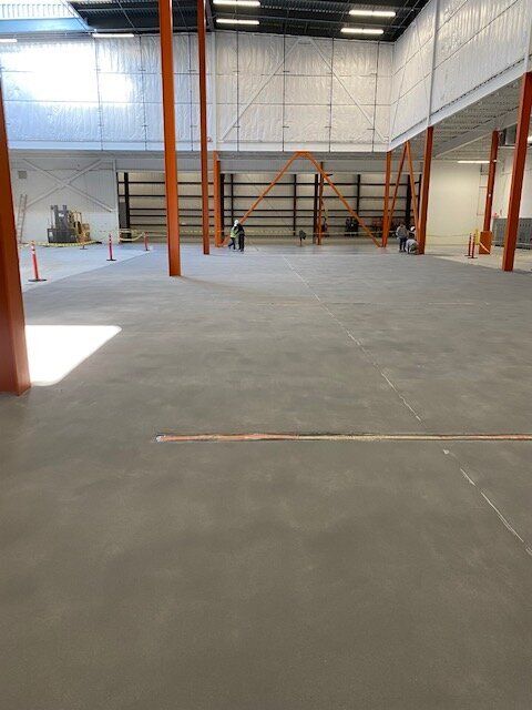 A large empty brewery with a concrete floor and orange pillars.