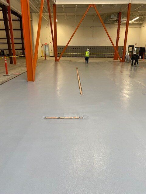 A large empty brewery with a concrete floor and orange pillars.