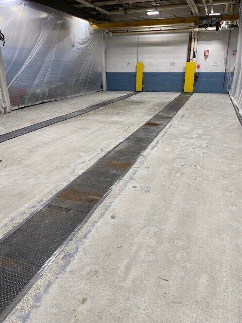 A large empty room with a concrete floor and a metal drain.