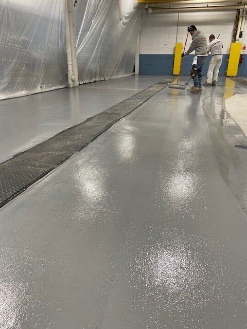 Two men are cleaning a concrete floor with a vacuum cleaner.