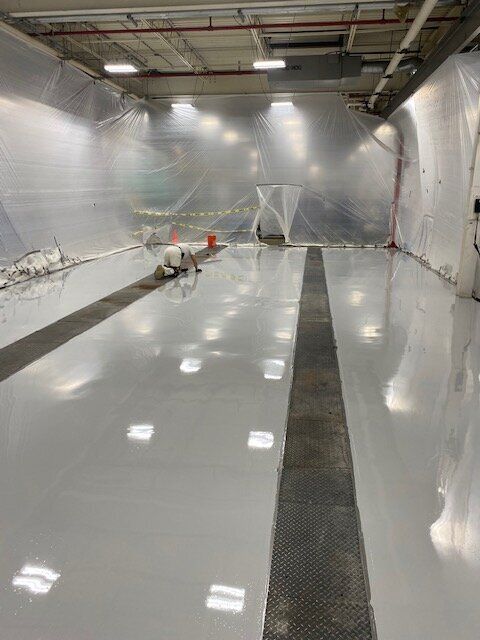 A person is kneeling on a white floor in a room covered in plastic.