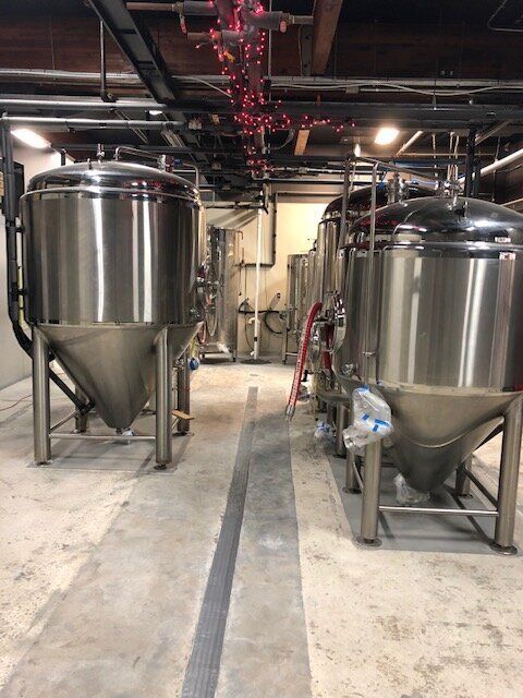 A row of stainless steel tanks are lined up in a brewery.