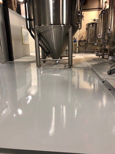 A large stainless steel tank is sitting on top of a white floor in a brewery.