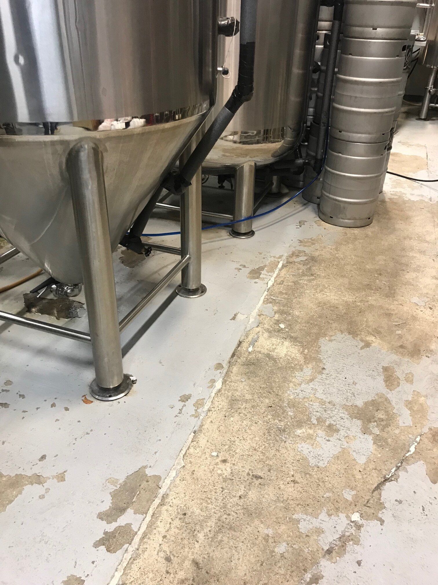 A dirty floor in a brewery with stainless steel tanks and kegs.