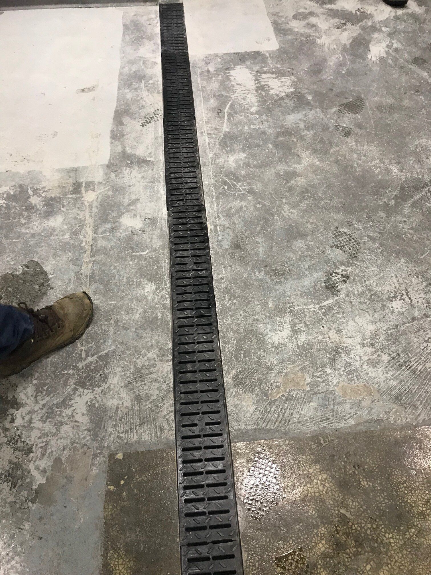 A person is standing next to a drain on a concrete floor.